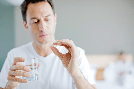 Man holding glass of water while looking at a pill in his hand