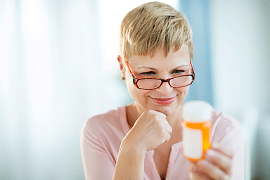 Mature woman with hand on chin reading label on prescription medicine bottle