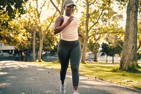 Happy woman wearing cap and jogging in park