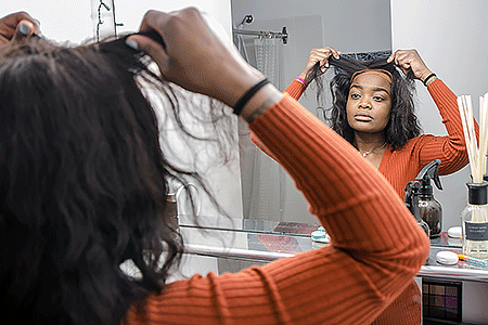 Woman putting on wig in front of mirror