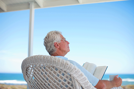 Senior man reading book on patio by the beach
