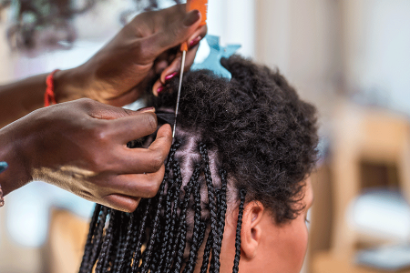 Hair stylist tightly braids client’s hair close to the scalp.