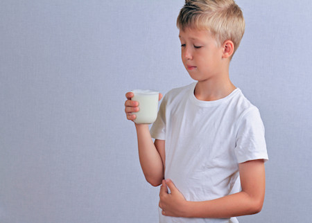 A boy with atopic dermatitis holding a hand on his belly because he has stomach pain, which can be a symptom of food allergy.  