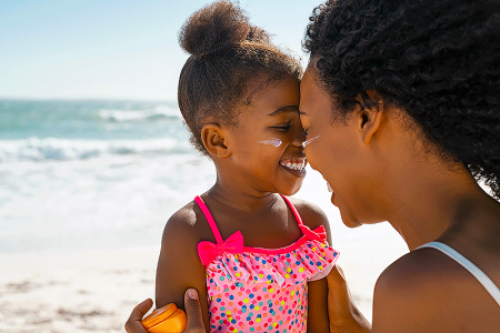 Mother hugging young daughter with sunscreen on their faces at the beach.