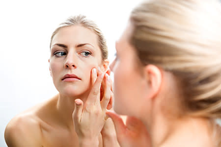 Woman examining skin on her face in the mirror