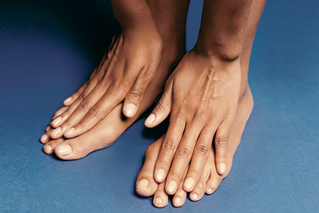 Woman placing her hands on the tops of her feet so that she can see all of her nails