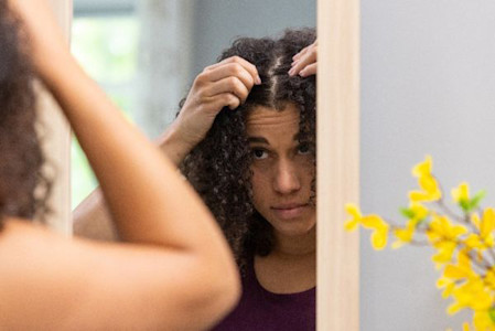 Woman checking scalp for hair loss in a mirror