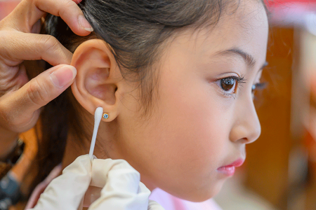 Mother cleaning her young daughter’s newly pierced ear