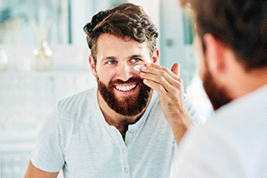 Happy man applying moisturizer to his face