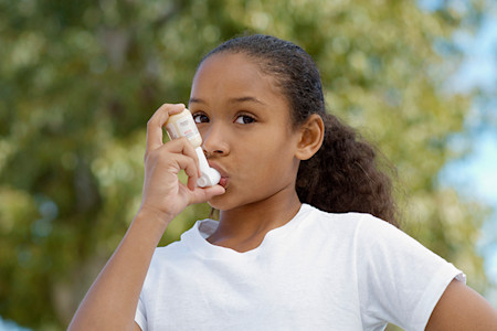 A girl is using an inhaler to control asthma, a condition that kids with atopic dermatitis have a greater risk of developing.