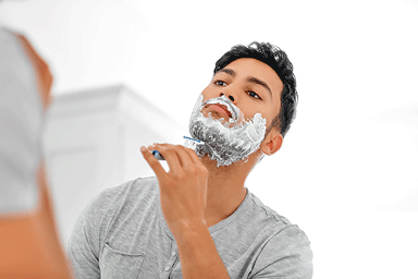 Close-up of a young man shaving his beard with a razor in his bathroom