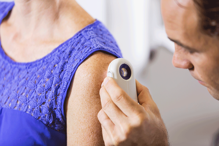 A dermatologist carefully examining the skin of a patient using a dermatoscope, looking for signs of skin cancer.