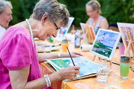 Side view of a happy senior woman smiling while drawing outdoors together with a group of retired women
