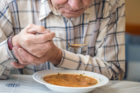 Man with Parkinson’s disease steadying his hand so he can eat soup