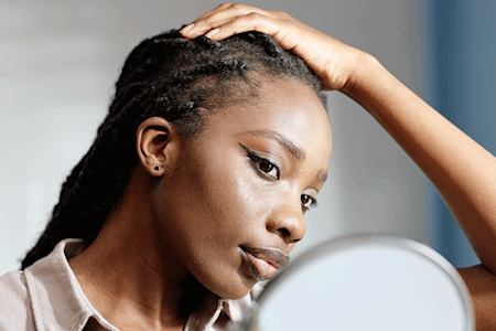 Woman looking at hairline in mirror. 