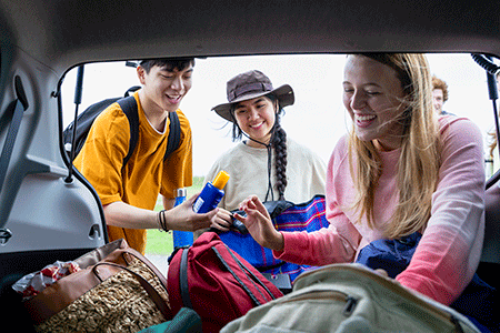 Three people retrieving luggage and sunscreen from the trunk of a car.
