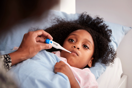 Sick child in bed taking temperature with thermometer