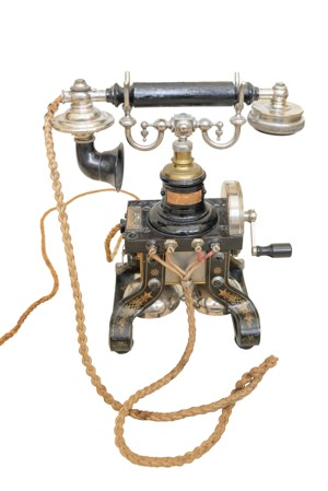 Antique rotary crank telephone with a separate earpiece and mouthpiece, ornate metal body, and a coiled cord, isolated on a white background.