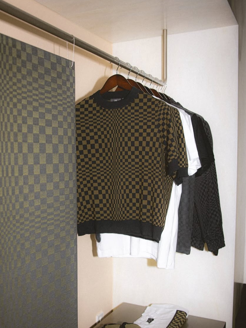 Checkered brown and black shirts on hangers in a closet, with matching fabric on the left wall.