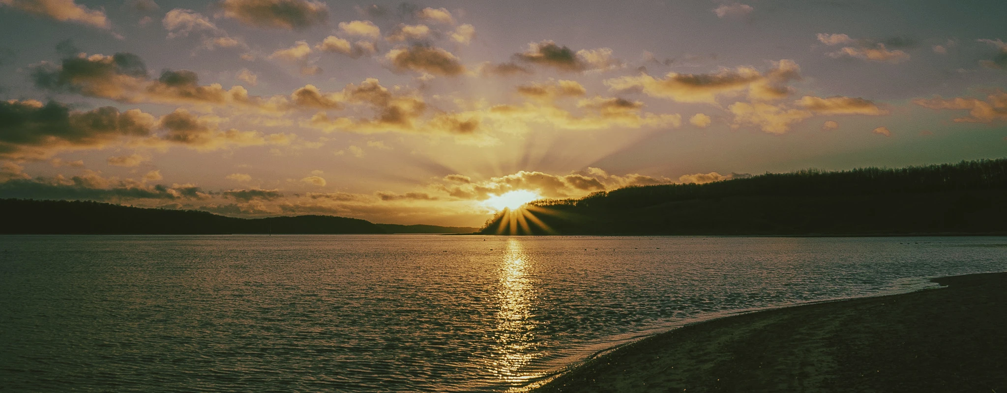 Ein wunderschöner Sonnenuntergang über dem Wasser. Man erkennt einzelne Lichtstrahlen der Sonne.