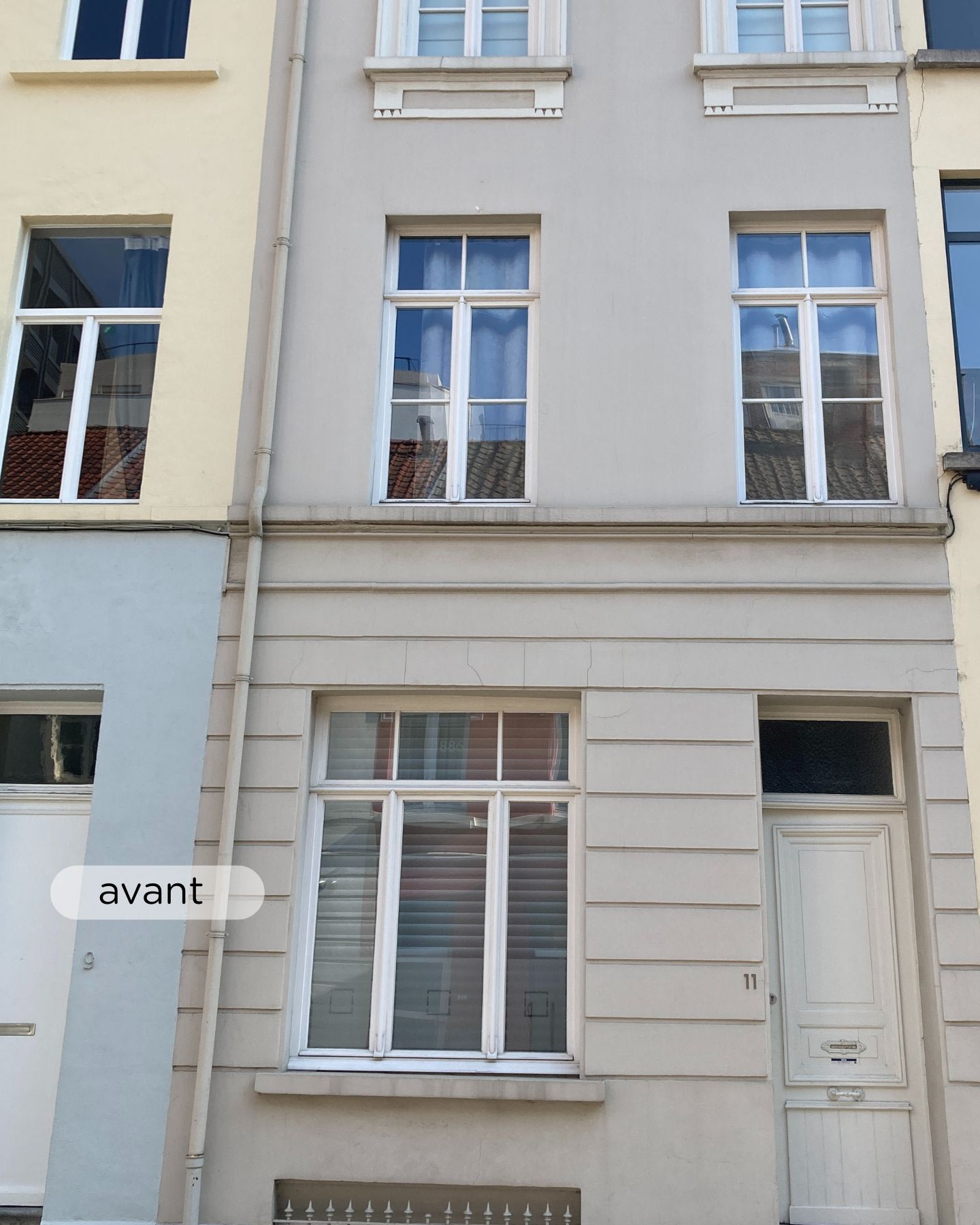 Maison de ville beige de trois étages avec des bandes décoratives blanches, deux fenêtres à l'étage supérieur, une grande fenêtre au rez-de-chaussée et une porte d'entrée blanche portant le numéro 11.