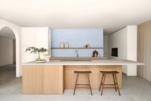Cuisine moderne avec îlot central, deux tabourets en bois, armoires en bois clair, mur d'accent bleu, étagères ouvertes et décoration minimaliste.