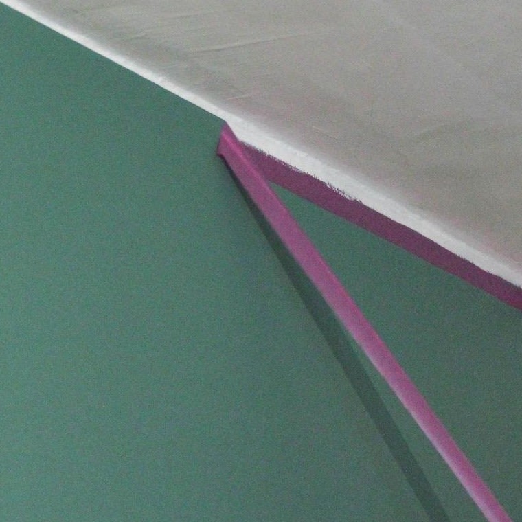 Een hoek van een kamer waarvan één muur groen is geschilderd en het plafond en de aangrenzende muur wit. Paarse schilderstape zorgt voor strakke randen langs de hoeken waar de muren en het plafond samenkomen.