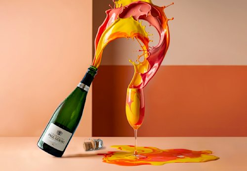 Une bouteille de champagne verse un liquide orange et jaune coloré dans un verre, avec des éclaboussures figées dans les airs et un bouchon posé sur la table.