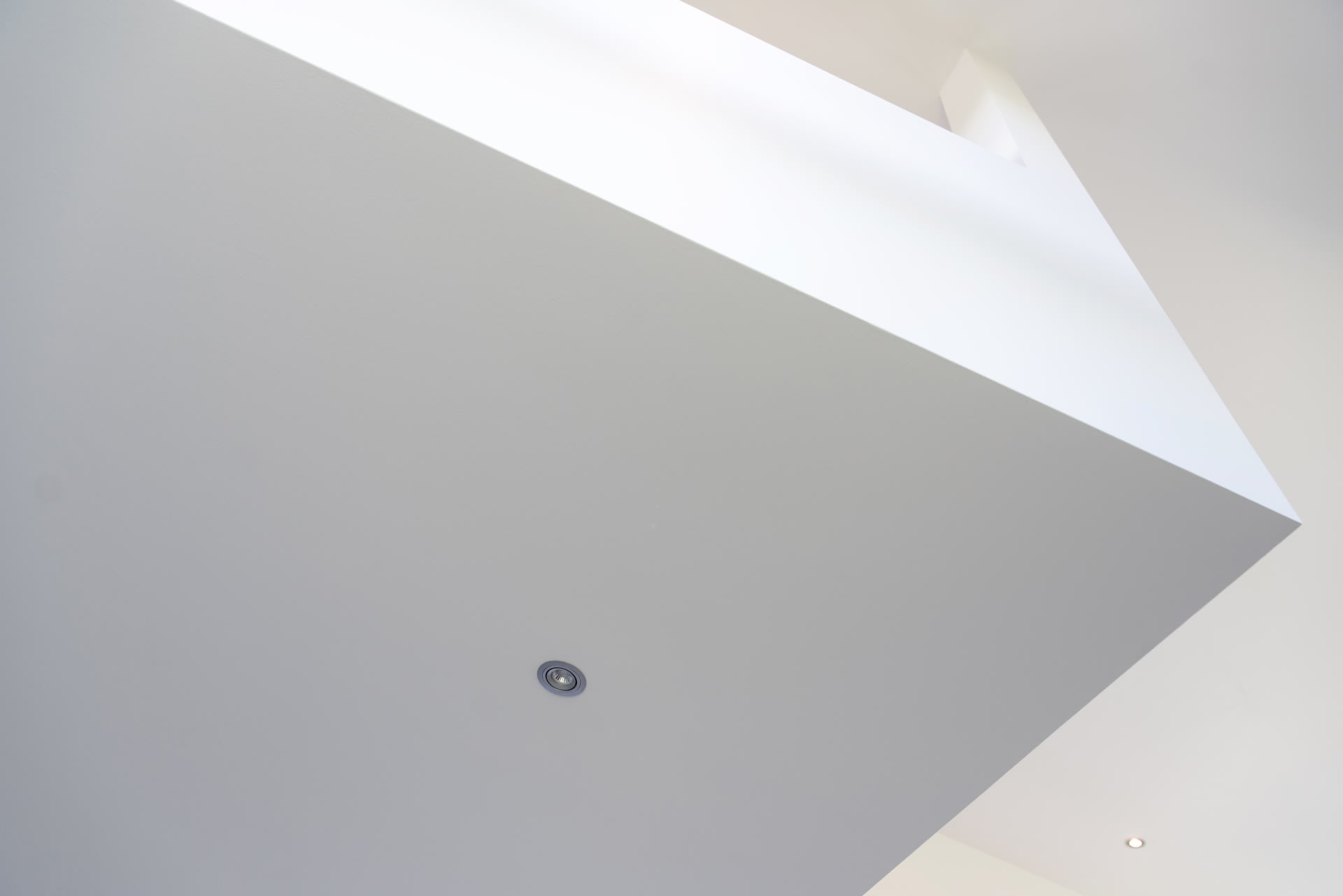 Un luminaire encastré au plafond est installé dans un plafond lisse et blanc aux lignes épurées et à l'architecture minimaliste.