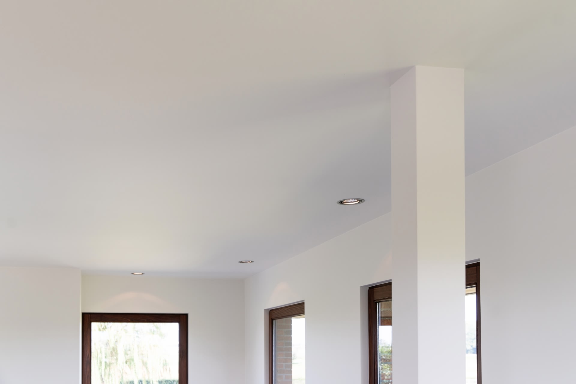 Plafond blanc et murs supérieurs d'un intérieur moderne avec éclairage encastré, grandes fenêtres avec cadres bruns et colonne carrée.
