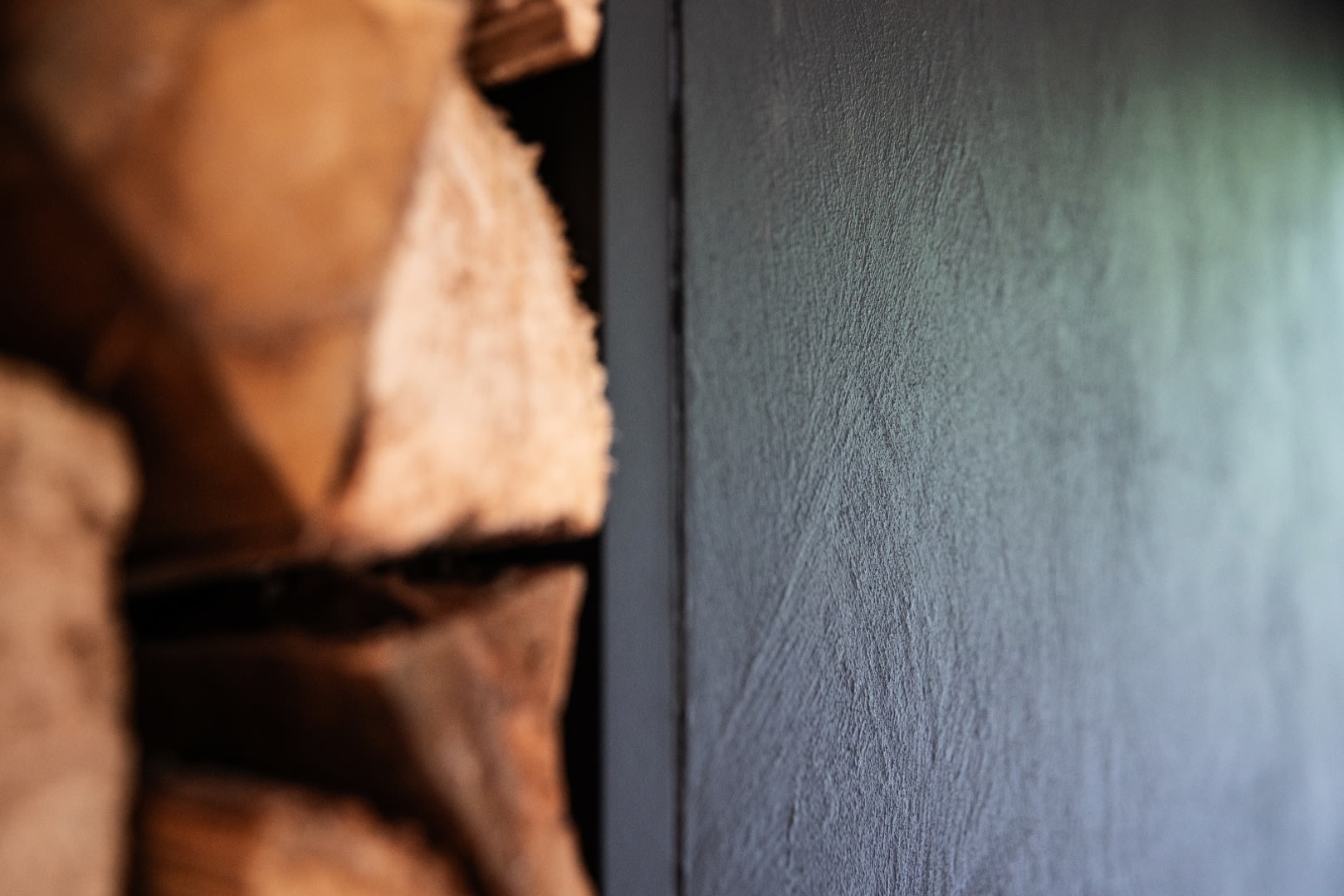 Gestapeld gezaagd brandhout naast een haardwand met zichtbare textuur, gefotografeerd in close-up.