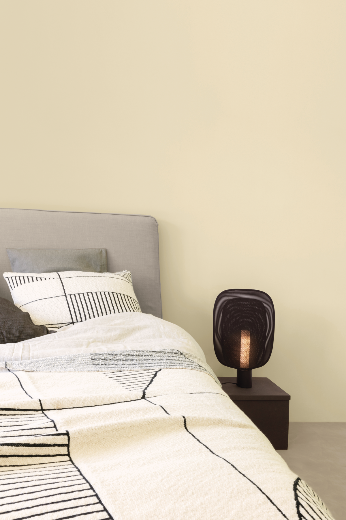 Colora – slaapkamer met beige muren, grijs bed en zwarte nachtkast en lamp