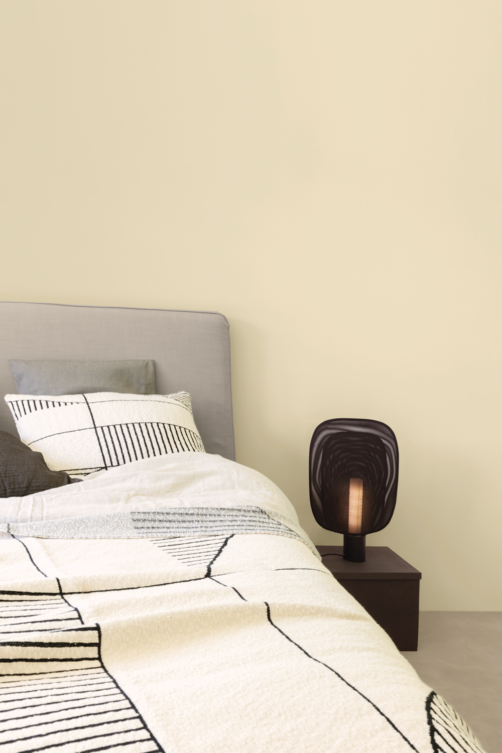 Colora – slaapkamer met beige muren, grijs bed en zwarte nachtkast en lamp
