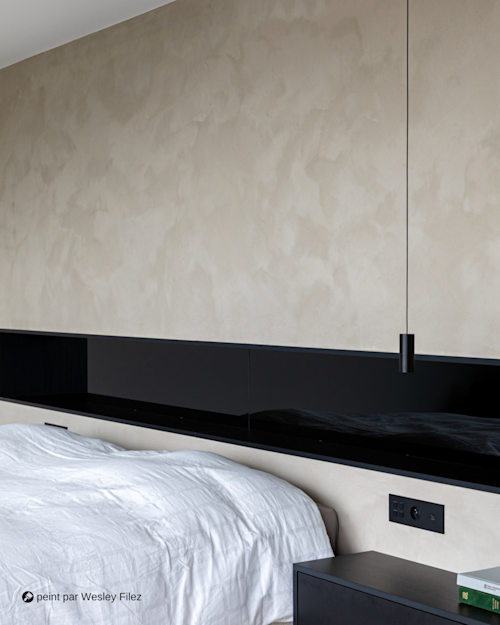 Une chambre moderne avec un mur beige texturé, une tête de lit en panneau noir, un lit blanc et une suspension noire suspendue.