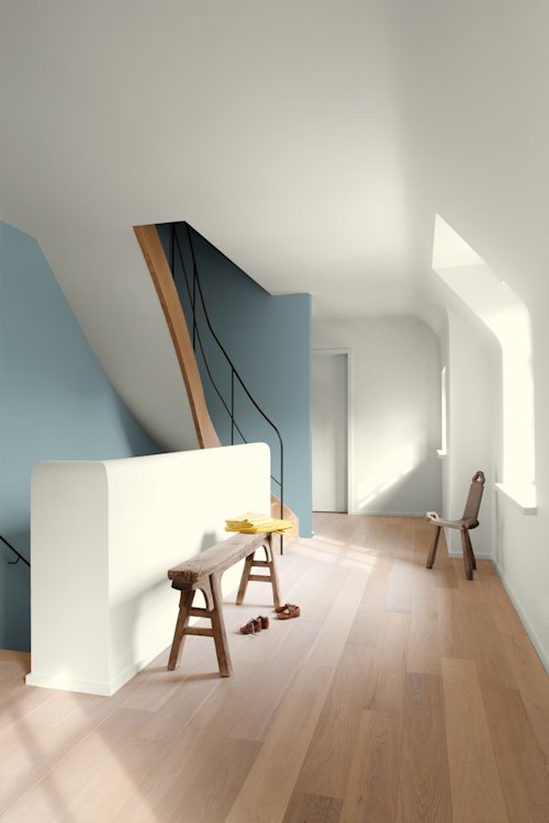 Een minimalistische hal met lichte houten vloeren, een houten bank met kleren en sandalen, een enkele stoel bij een raam en een gebogen trap met een zwarte leuning.