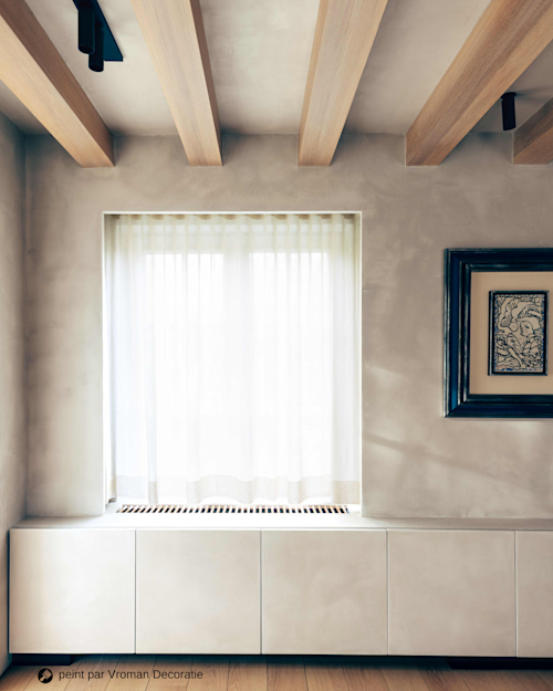 Espace de vie lumineux avec des murs beiges, des rideaux blancs, des peintures noires et des poutres en bois clair