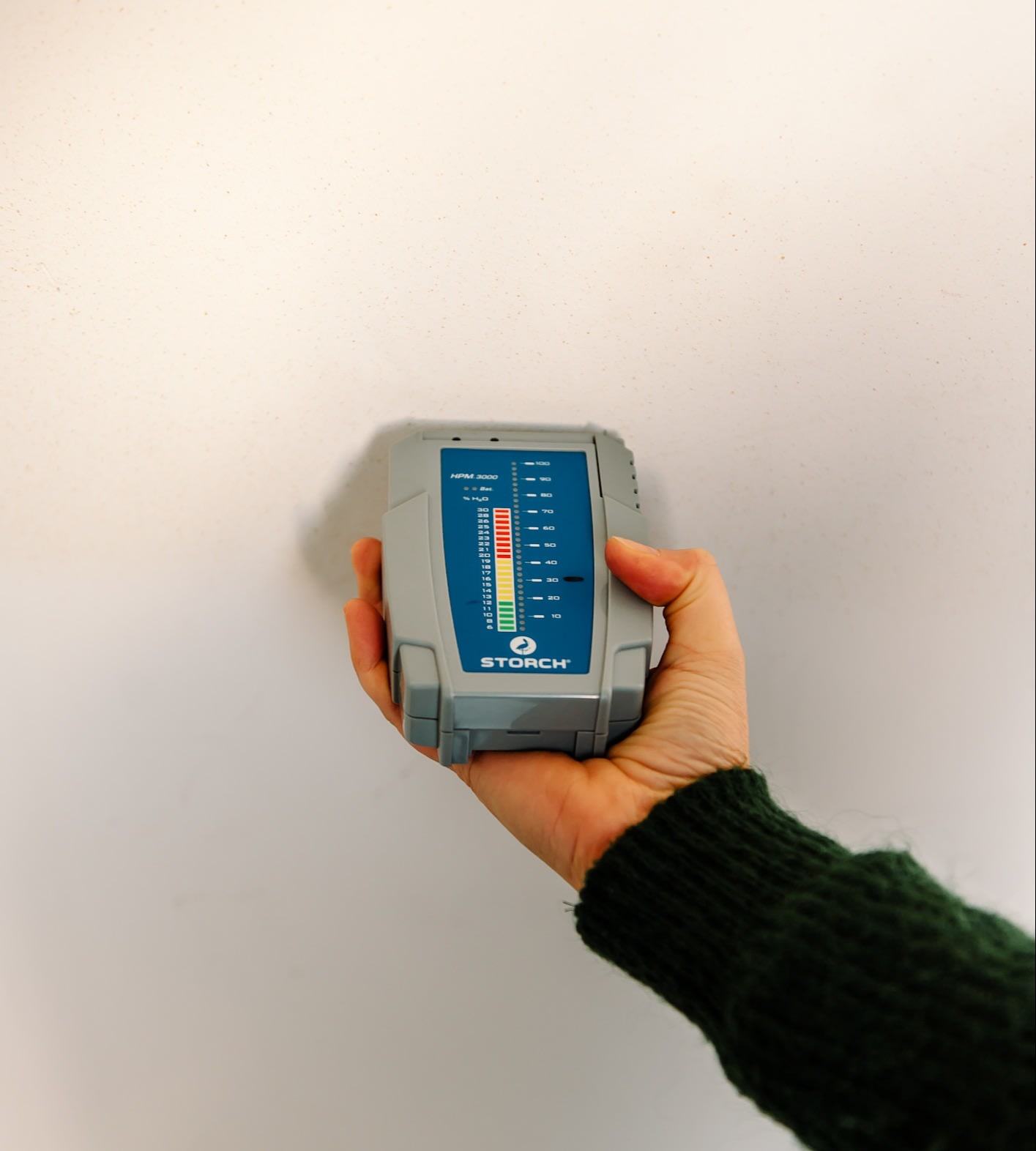 Persoon die vochtmeter tegen een witte muur houdt