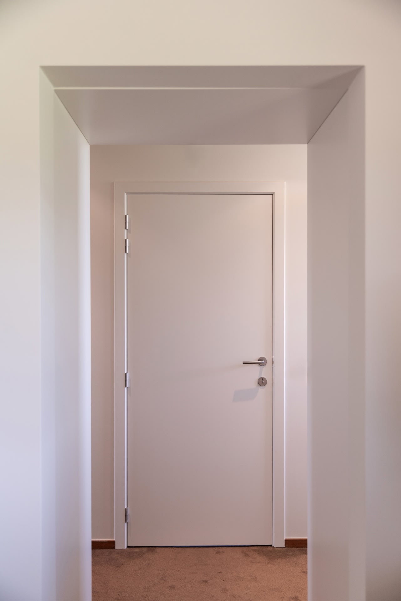 Une porte intérieure blanche fermée encadrée par une ouverture blanche, avec une poignée métallique et un tapis beige visible.