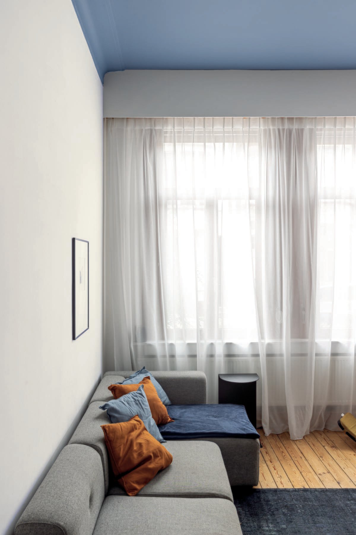 woonkamer met witte muren en blauw plafond, zetel en gekleurde kussens - colora magazine herfst 2022