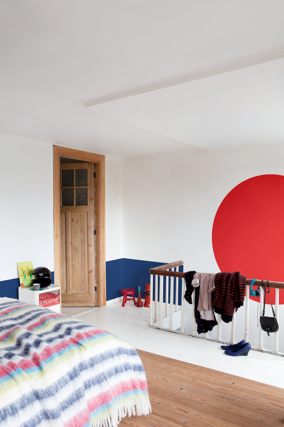 Colora-slaapkamer met witte muren, donkerblauwe balk onderaan de muur en grote rode cirkel op de muur