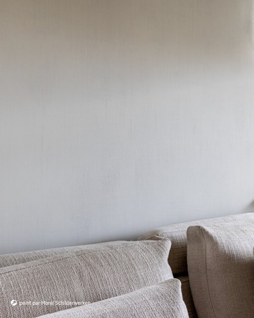 Gros plan sur un canapé beige texturé avec des coussins, devant un mur uni gris clair, partiellement éclairé par une douce lumière naturelle provenant du coin supérieur droit.