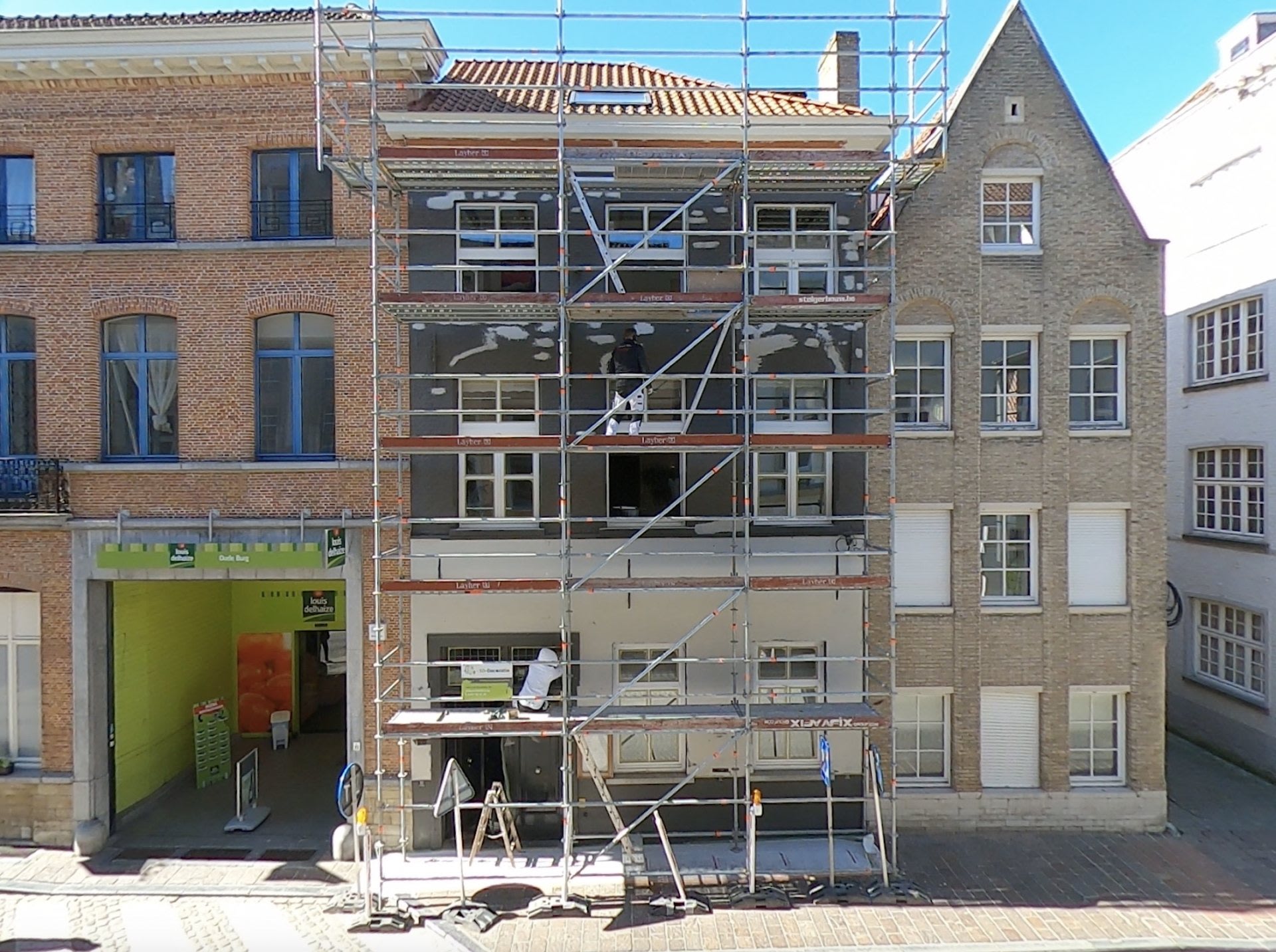 Un bâtiment de trois étages en cours de rénovation est recouvert d'échafaudages ; les bâtiments adjacents sont visibles des deux côtés.