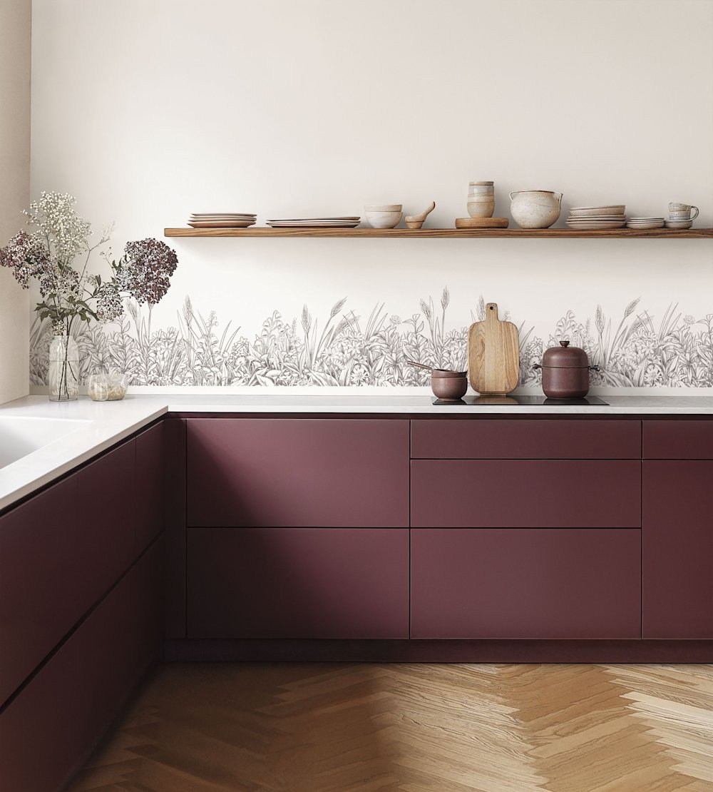 papier peint - cuisine - Caselio - Kitchen box - KBO106960936 - blanc - noir  - Mur blanc avec motif floral noir, armoires de cuisine rouge vin, sol en bois, pots en terre cuite.