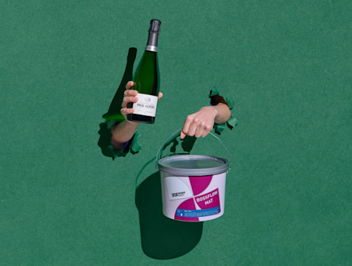 Deux mains se détachent sur un fond vert : l'une tient une bouteille de vin, l'autre un seau de peinture portant l'inscription « BOSSFLOW MAT ». Les ombres des bras sont visibles sur la surface.