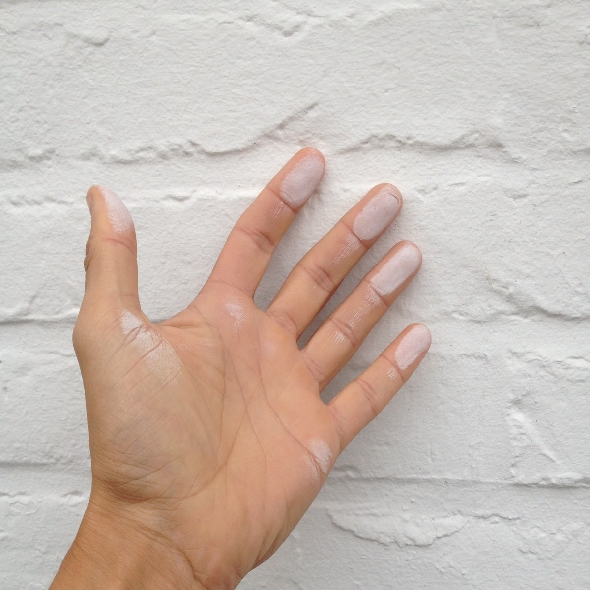 Een hand met sporen van witte verf op de vingers wordt open gehouden tegen een witte bakstenen muur. 