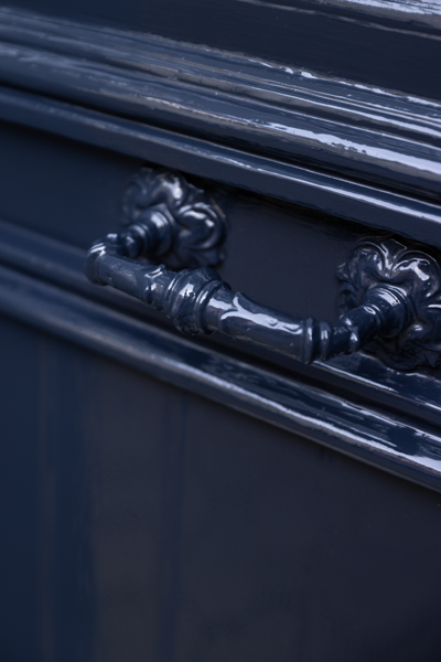 Close-up van een sierlijk, donkerblauw geschilderd metalen handvat bevestigd aan een bijpassend paneel met decoratieve achterplaten.