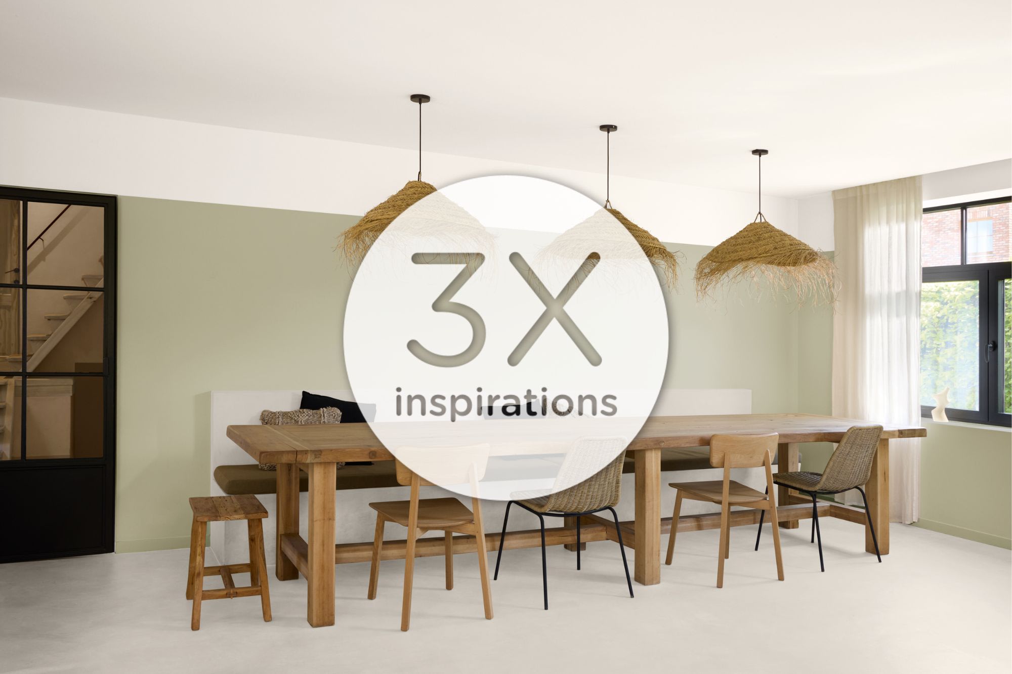Salle à manger moderne avec une table en bois, des chaises assorties, des suspensions tressées, un mur d’accent vert clair et un grand plateau rond portant l’inscription « 3x anders » au centre.