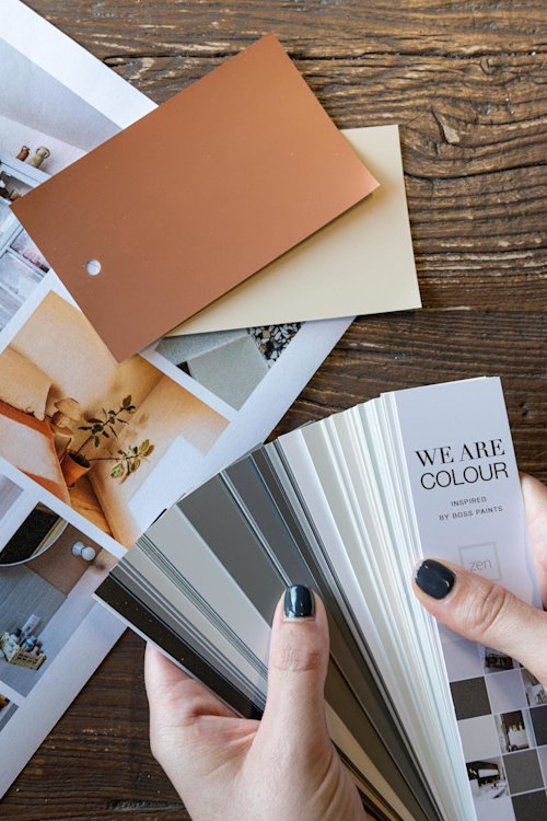 persoon die kleurwaaier vasthoudt in handen met moodboard en kleurkaartjes op de tafel