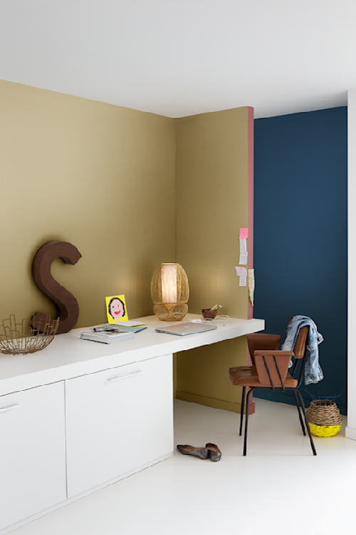De muur achter het bureau in een geelgoudkleurige metallic chic voelt heel luxueus. De blauwe verfkleur van de muur in de hal maakt een warm contrast.