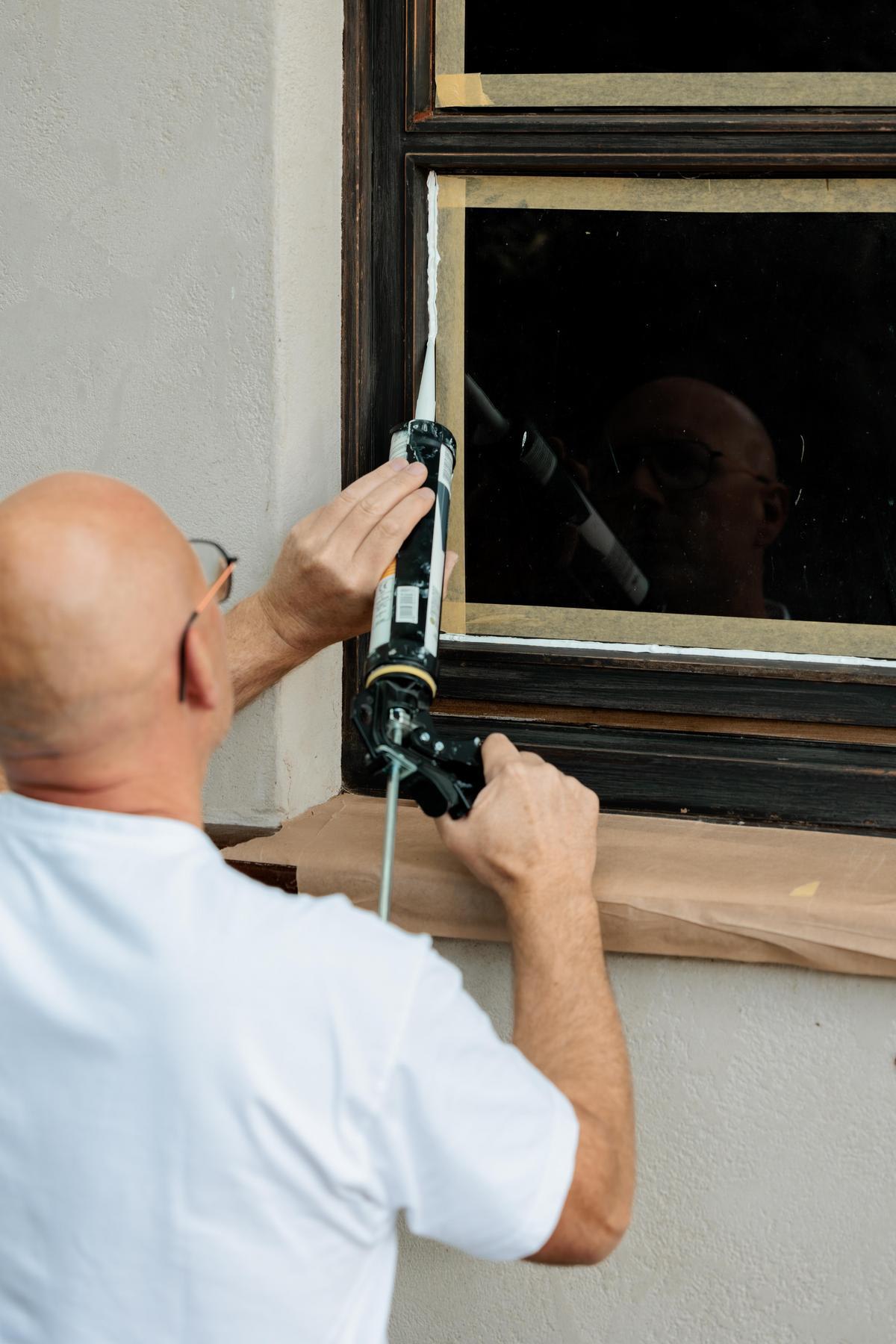 Iemand brengt witte kit aan op de rand van een raamkozijn met een kitpistool.